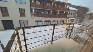 A balcony with a metal railing, snow-covered ground, and a building with multiple windows and balconies in the background. - Korte Hotel Sleeps 14 With Courtyard (Mestia)