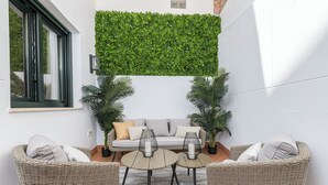 A cozy outdoor seating area with wicker furniture, a green vertical garden, and a white wall. - Solaga - Cinteria (Málaga)