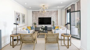 A modern living room with a sofa set, two side tables, a coffee table, and a large flat-screen TV mounted on the wall. - Solaga - Cinteria (Málaga)