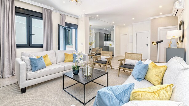 A modern living room with a sofa, coffee table, and chairs. There is a kitchen in the background. - Solaga - Cinteria (Málaga)