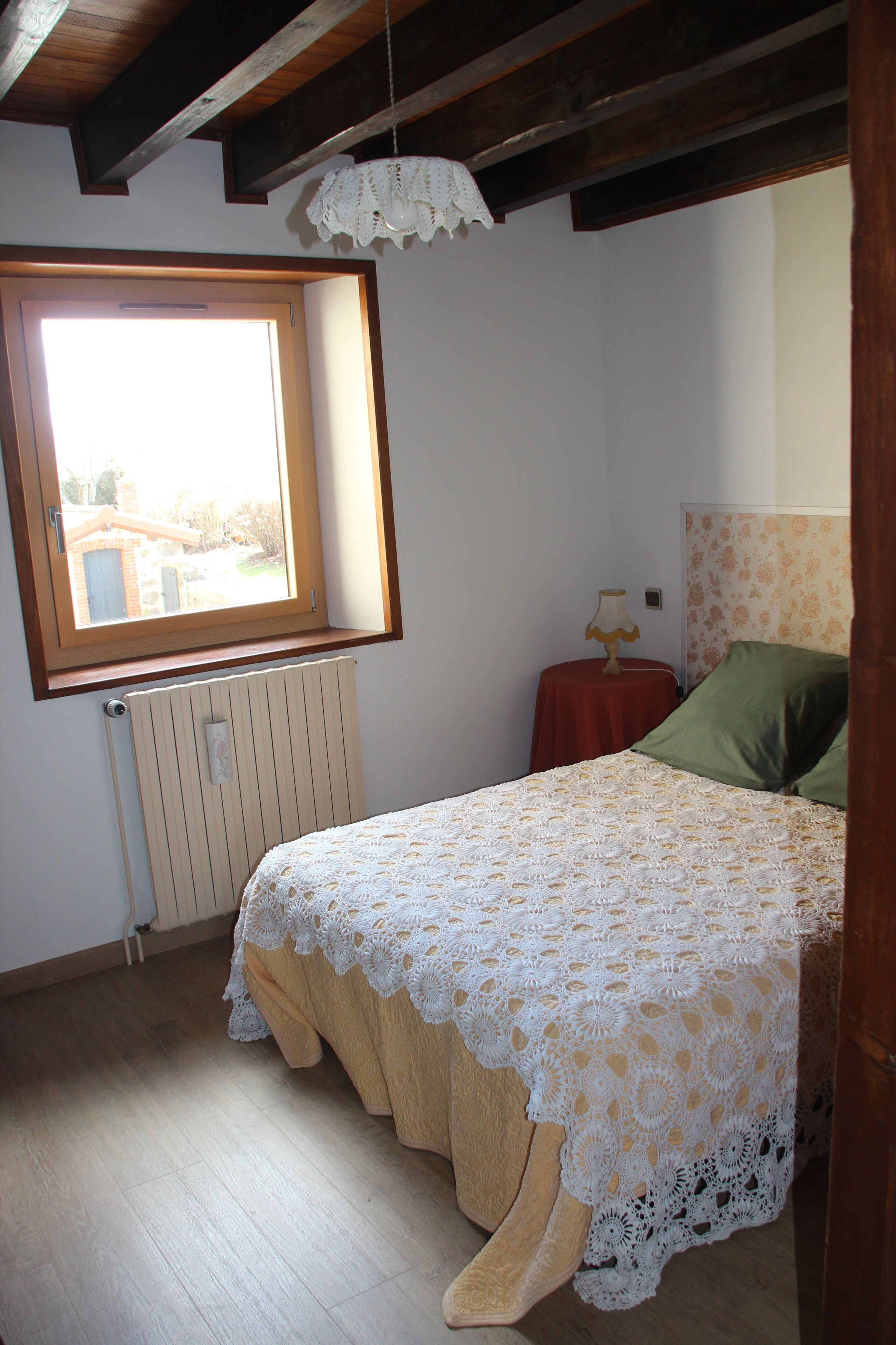 Een slaapkamer met een bed, een raam, een radiator en een nachtkastje met een lamp.