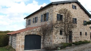 A stone building with a large garage door, multiple windows, and a sloped roof. - Stone and wood house (Saint-Pal-de-Chalencon)