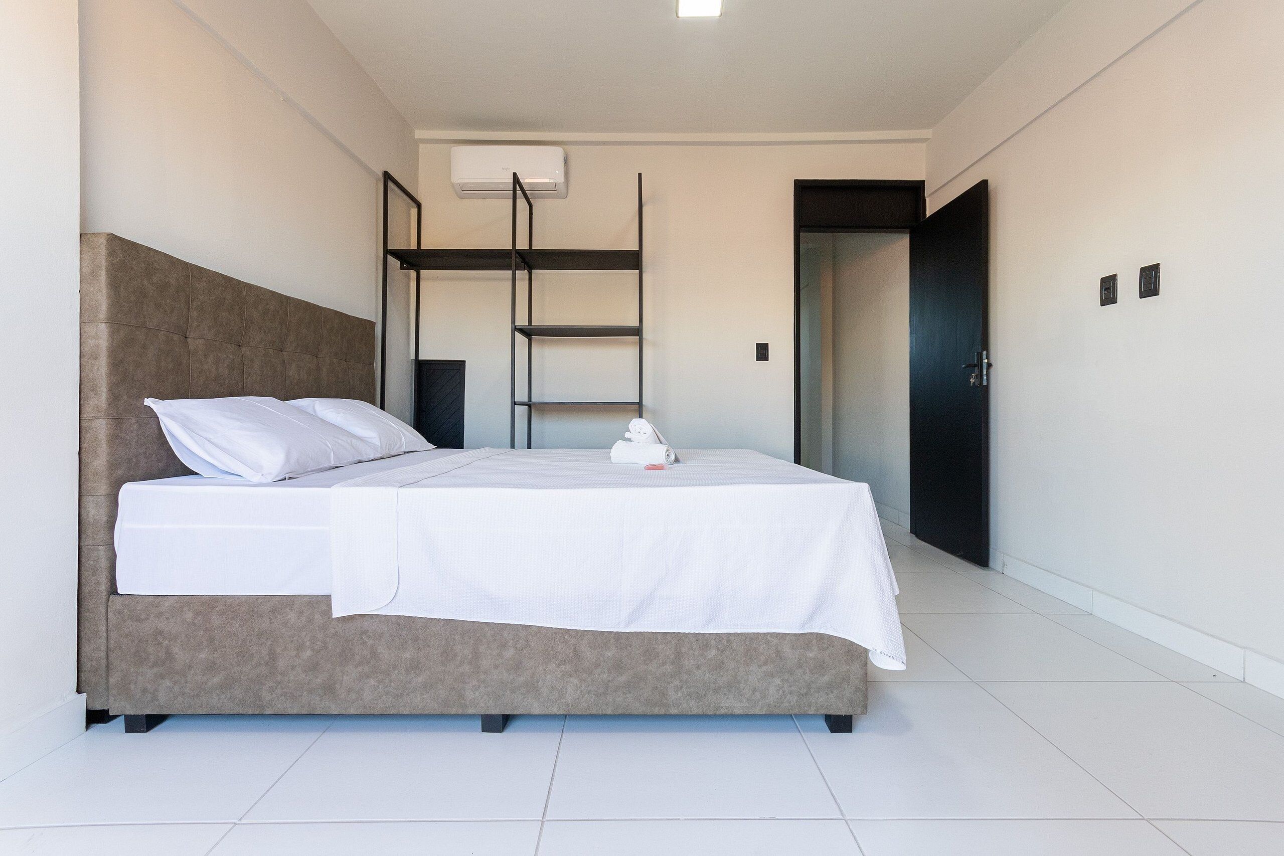 Quarto moderno com uma cama grande, uma estante embutida e uma porta que dá para outro cômodo.
