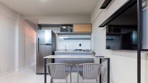 Una cocina moderna con un refrigerador de acero inoxidable, un microondas y un armario de madera sobre la encimera. Hay dos sillas en una mesa pequeña.
