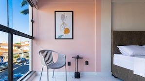 Una habitación de hotel moderna con una cama, una silla, una mesita y una obra de arte enmarcada en la pared.