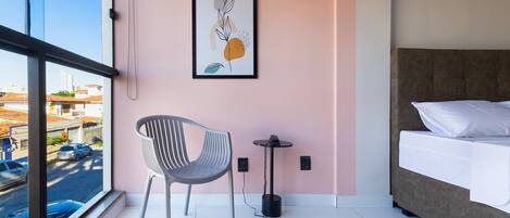 A modern hotel room with a bed, a chair, a small table, and a framed artwork on the wall.