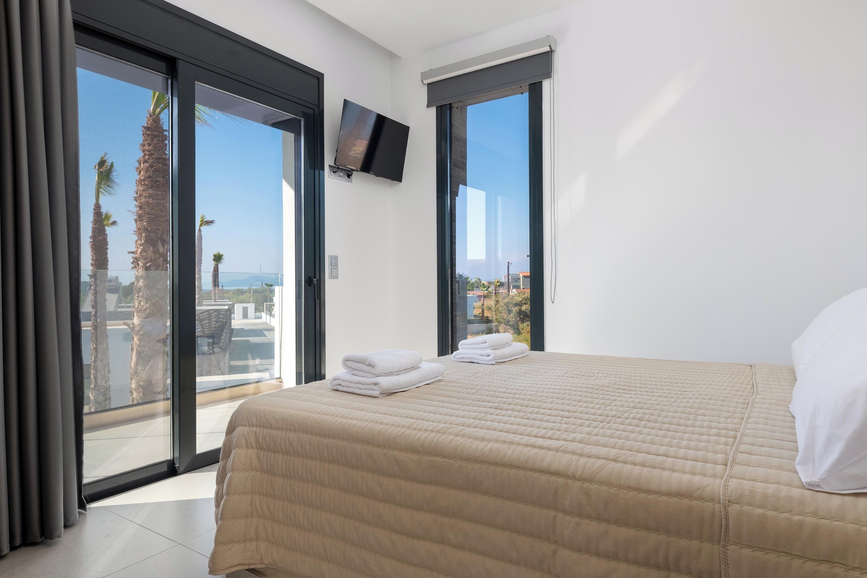 Une chambre avec un lit, une télévision et un balcon agrémenté de palmiers.