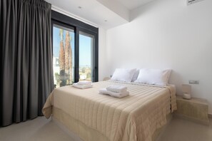 A bedroom with a large bed, a nightstand, a lamp, and a window with curtains.