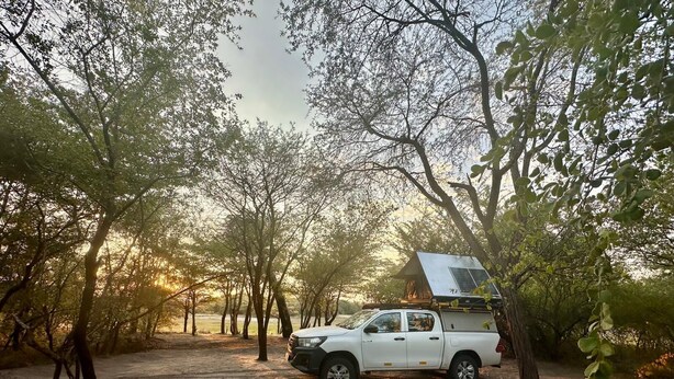 A white pickup truck parked on a dirt path surrounded by trees. - Kayubo Campsite (Kongola)