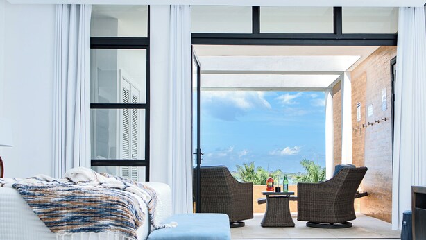 A modern bedroom with a bed, a small table, two chairs, and a view of the sea. - Welcome N/H Villa Paradise in enchanting Reading, Montego Bay with AC, Gym, WiFi (Reading)