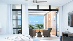 A modern hotel room with a large bed, a balcony with wicker furniture, and a TV on the wall. - Welcome N/H Villa Paradise in enchanting Reading, Montego Bay with AC, Gym, WiFi (Reading)