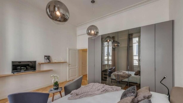 Een moderne slaapkamer met een groot bed, een televisie op een plank, een spiegel en een stoel.