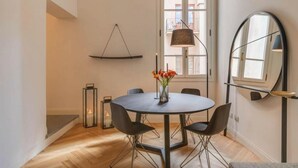 Een moderne eetruimte met een ronde tafel, zwarte stoelen, een vaas met bloemen, een hanglamp en een grote spiegel.
