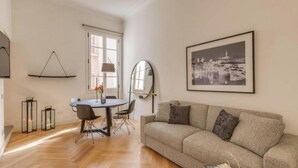 Een moderne woonkamer met een bank, een eettafel met stoelen, een lamp en een ingelijste foto aan de muur.