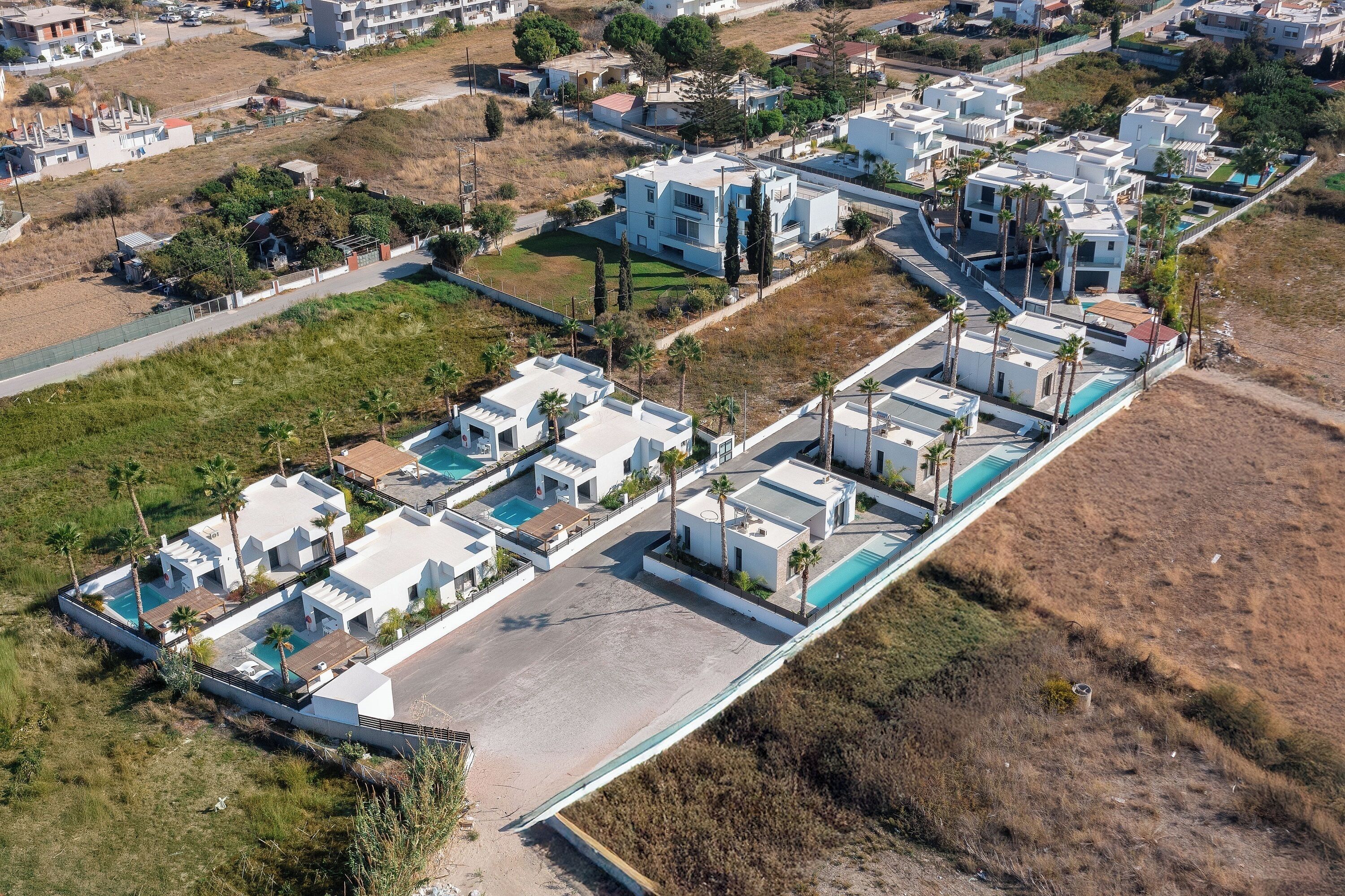 Ett flygbildsbild av ett bostadsområde med moderna hus, en swimmingpool och ett stort, öppet område.