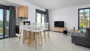 Una sala de estar moderna con un sofá gris, un televisor y un comedor con sillas blancas y un mueble de madera.