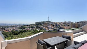 Terraza en la azotea con mesa y sillas, ofreciendo vistas panorámicas de un paisaje urbano con edificios y una torre.