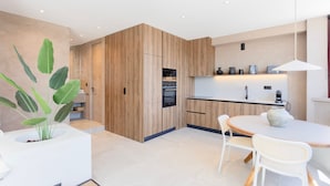 Cocina moderna con armarios de madera, horno integrado y comedor con una mesa y sillas redondas.