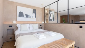 Una habitación de hotel moderna con una cama grande, una mesita de noche, una obra de arte en la pared y un espejo grande que refleja la habitación.
