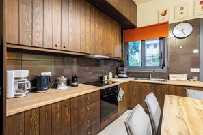 Eine moderne Küche mit Holzausstattung, einem eingebauten Backofen, einer Kaffeemaschine und einem Fenster mit Blick nach draußen.