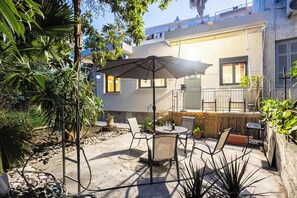 An outdoor patio area with a table and chairs, surrounded by plants and a building in the background. - Jeannette's Seaside Getaway - Kalamata Urban Gem (Kalamata)