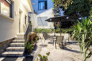Eine Terrasse mit Gartenmöbeln, ein Tisch mit Flasche und Glas sowie eine Treppe zu einer oberen Ebene.