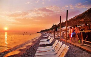 Une plage avec des transats et des parasols, un coucher de soleil, et des gens qui se détendent.
