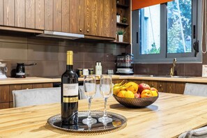 A modern kitchen with wooden cabinets, a wine bottle, two glasses, and a fruit bowl on the counter. - Jeannette's Seaside Getaway - Kalamata Urban Gem (Kalamata)
