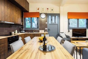 Eine moderne Küche mit Holzausstattung, einem Esstisch mit Stühlen, einem Fernseher und einem Fenster mit orangefarbenen Jalousien.