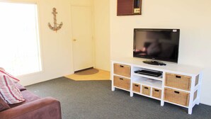 A living room with a television, a sofa, a door, and a wall-mounted radio. - Alton Seas 67 Hargreaves Rd, Middleton (Middleton)