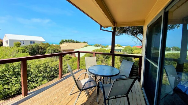 Une terrasse en bois avec une table et des chaises, offrant une vue sur un quartier résidentiel et la mer.