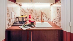 Une cuisine compacte dotée d’un crédence en marbre, d’une plaque de cuisson à induction en acier inoxydable, d’un évier et de meubles de rangement en bois.
