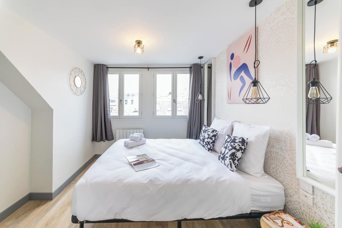 A modern hotel room with a large bed, a view of the city through the windows, and a decorative wall piece.