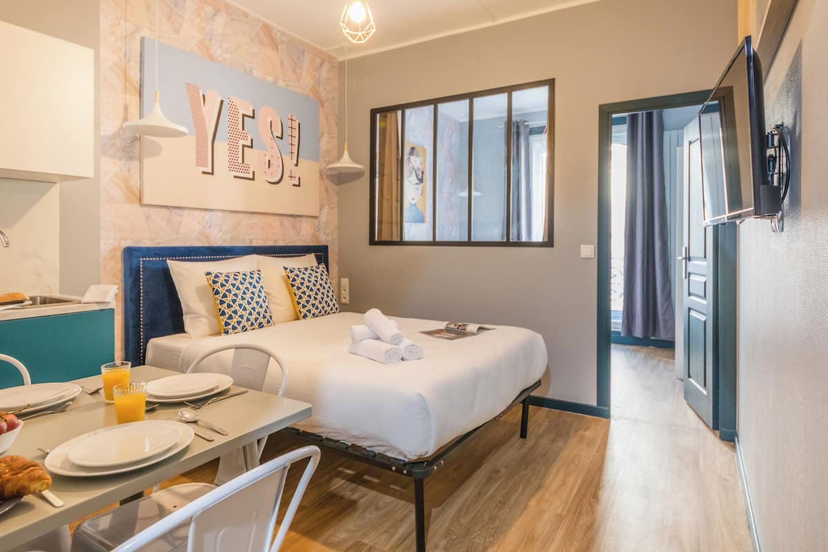 Une chambre d’hôtel avec un lit, une table à manger avec des aliments pour le petit-déjeuner, une télévision et une fenêtre avec des rideaux.