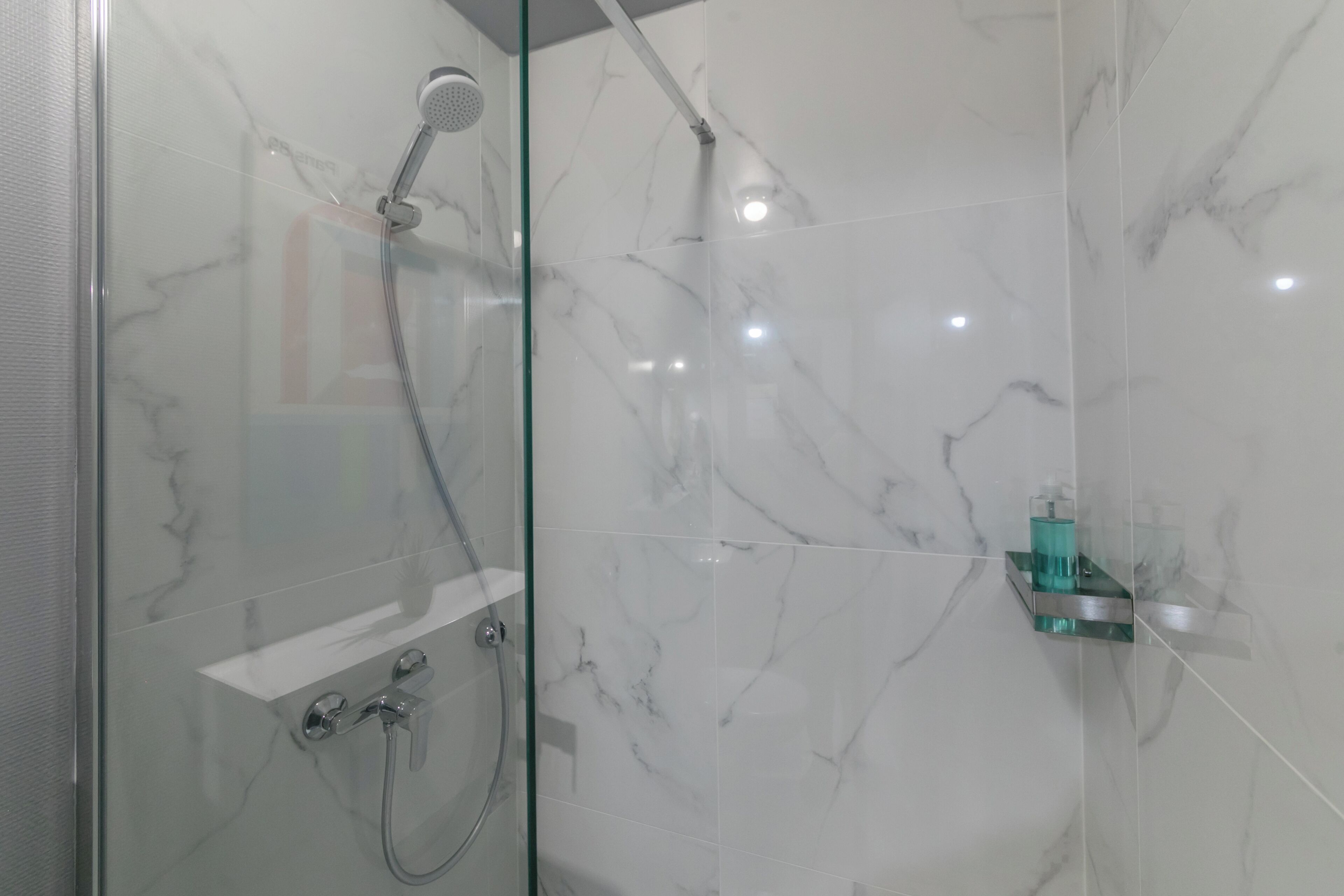 Un baño moderno con ducha acristalada, baldosas de mármol y un pequeño estante con artículos de aseo.