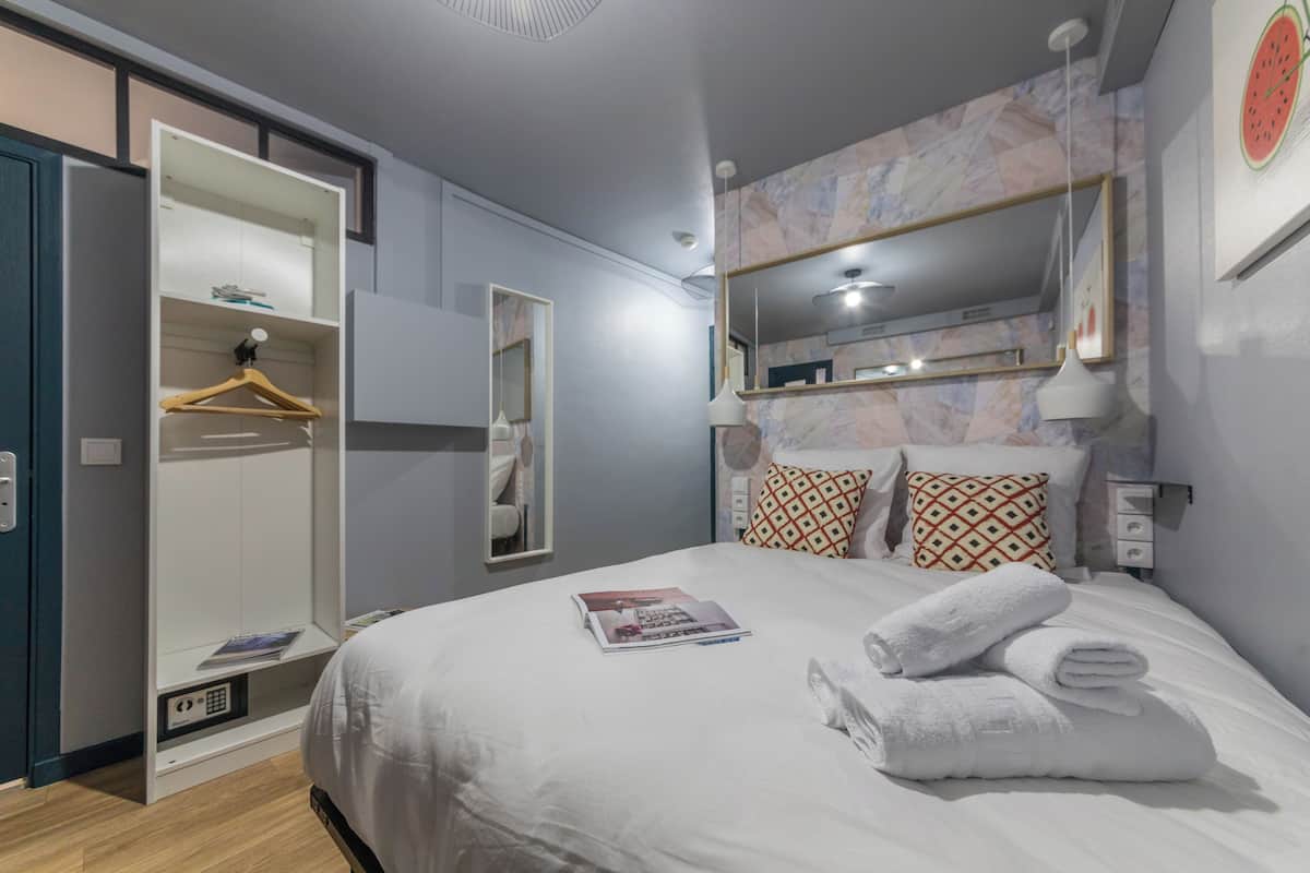 Une chambre moderne avec un lit, une armoire, un miroir et un mur orné d’une horloge.