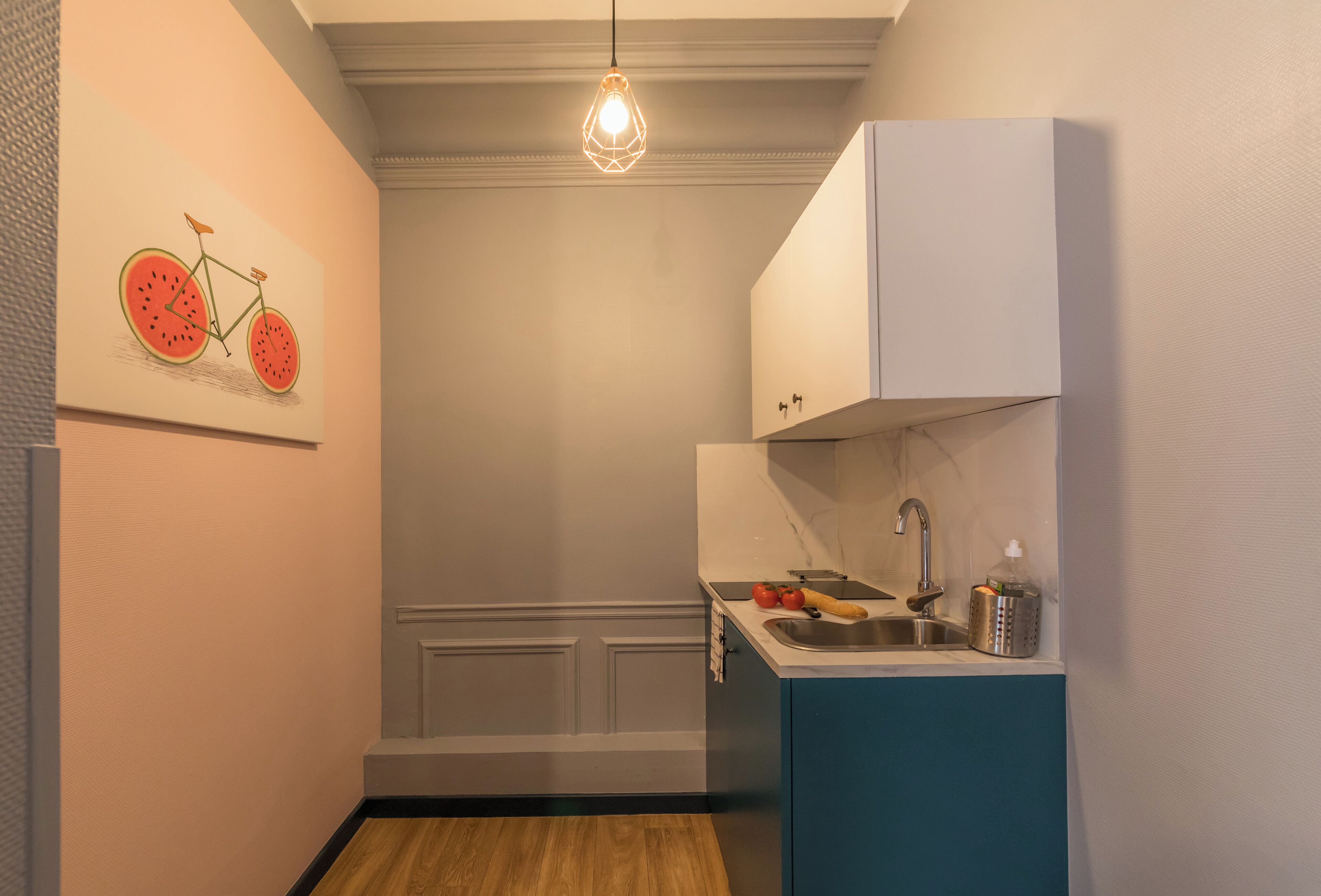 Une cuisine de taille réduite, équipée d’un évier, de placards et d’un luminaire suspendu.