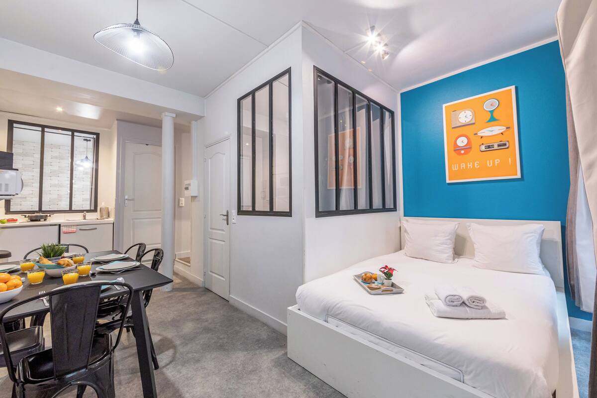 A modern hotel room with a large bed, a dining area with a table and chairs, and a bright blue accent wall.