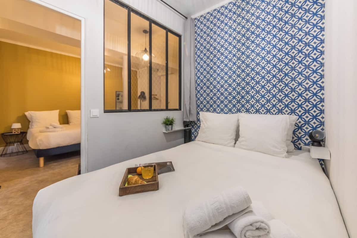 A hotel room with a bed, a window, a patterned wall, and a small table with a tray of food.