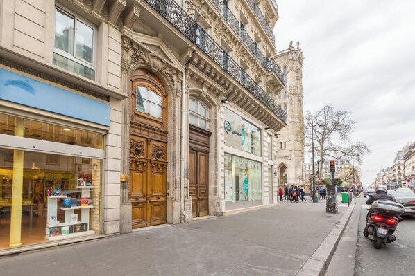 A street view with a building featuring ornate wooden doors and a storefront with a blue awning. - WS Hôtel de Ville - Le Marais (Paris)