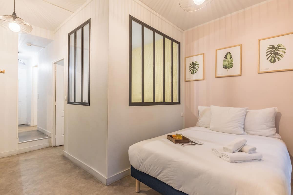 A hotel room with a bed, a tray with towels, and framed plant prints on the wall.