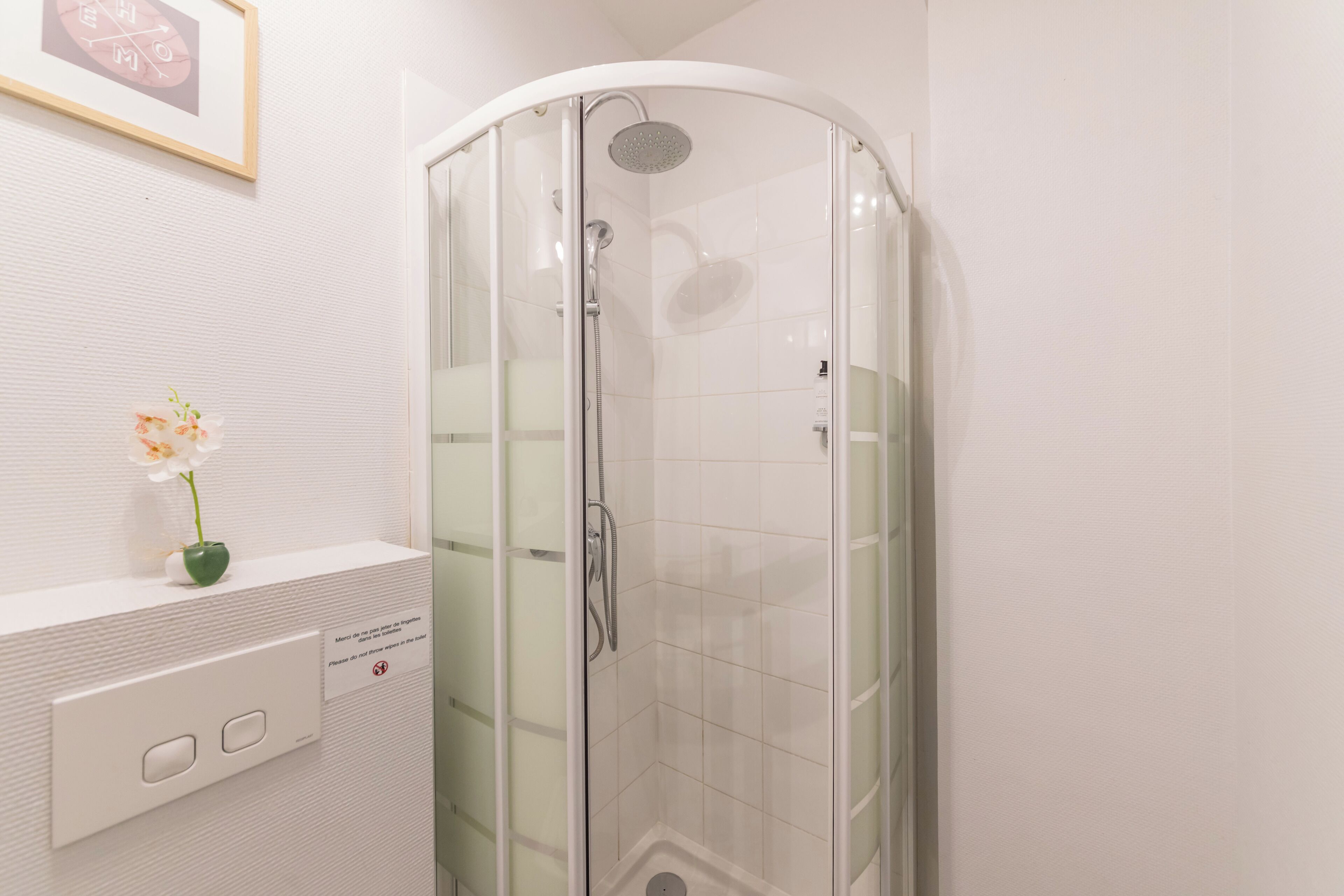 A modern bathroom with a glass-enclosed shower, a white sink, and a small vase with flowers.