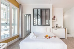 Habitación de hotel con una cama grande, un escritorio con microondas y vistas a la ciudad a través de amplios ventanales.
