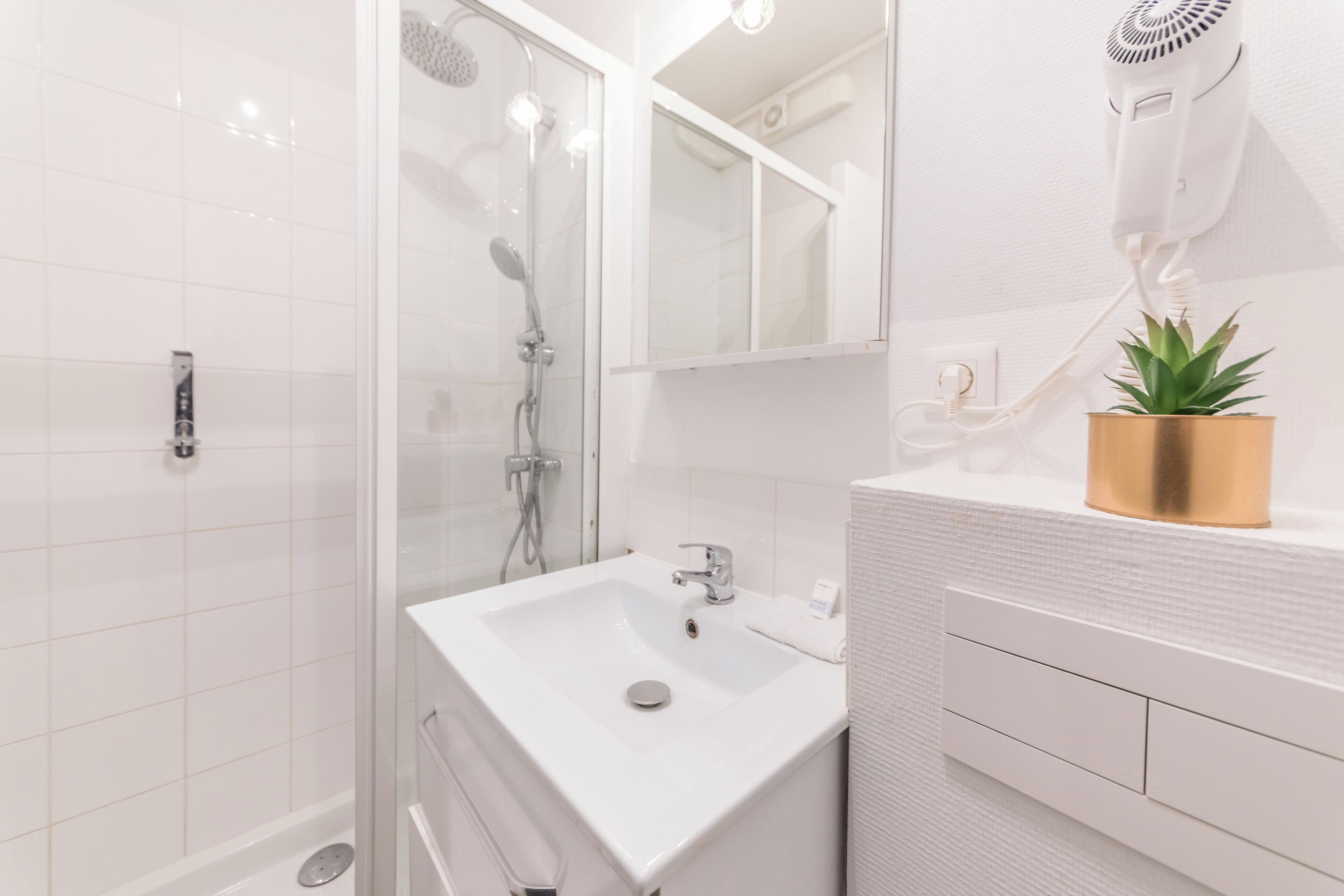 A modern bathroom with a glass-enclosed shower, a white sink, and a hairdryer mounted on the wall.
