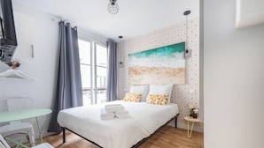 Quarto com cama, mesa, cadeiras, um quadro e janela com cortinas.