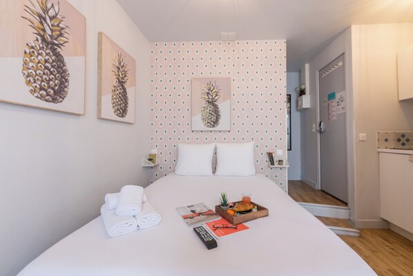 Un letto rifatto con cura, asciugamani, un vassoio con cibo, un telecomando e un'opera d'arte con ananas sulla parete.