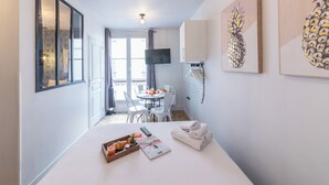Quarto de hotel com cama, área de refeições com mesa e cadeiras, TV fixada na parede e obras de arte nas paredes.