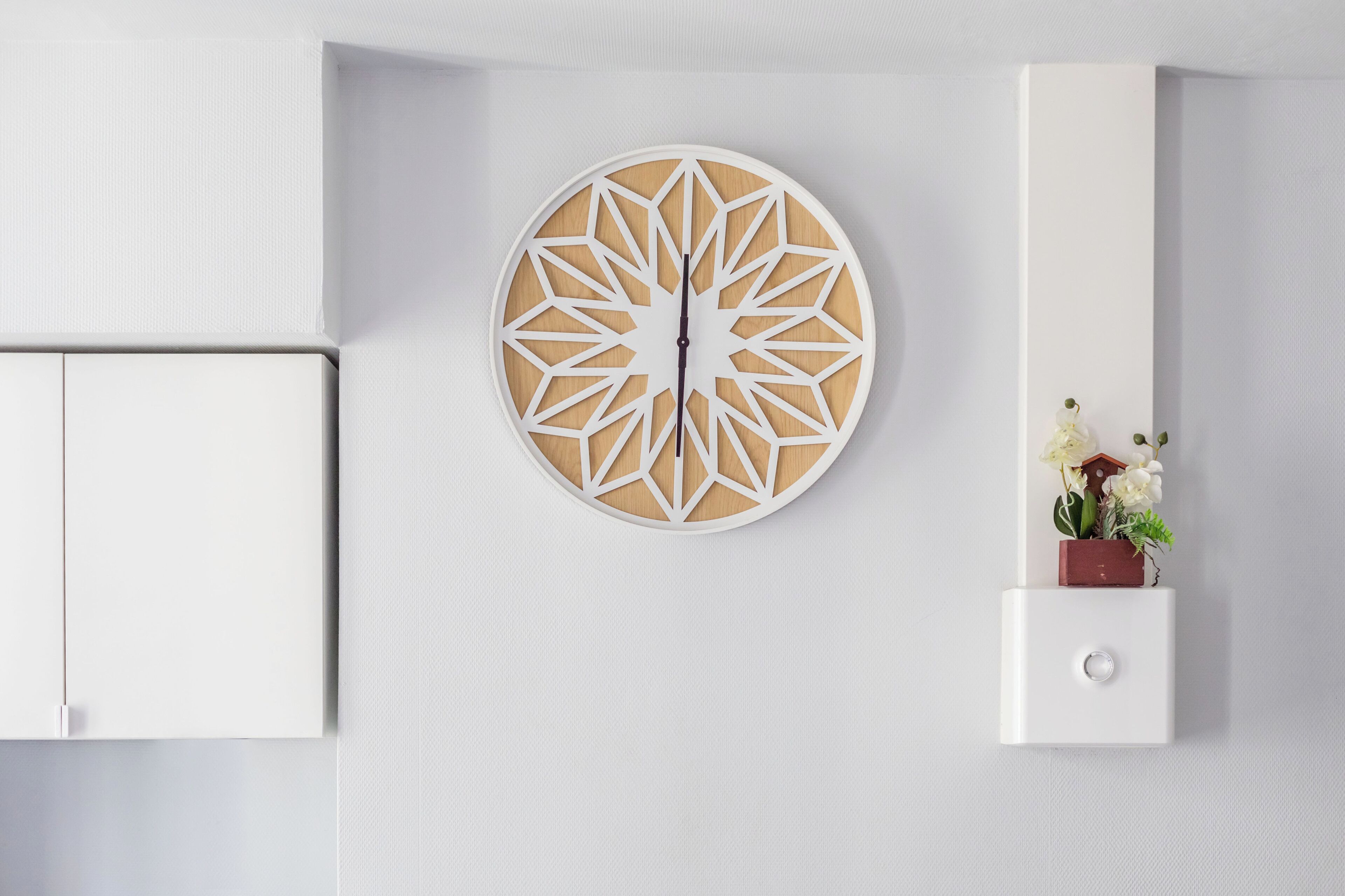 Un mur moderne agrémenté d’une horloge géométrique, d’une petite plante et d’un meuble blanc.