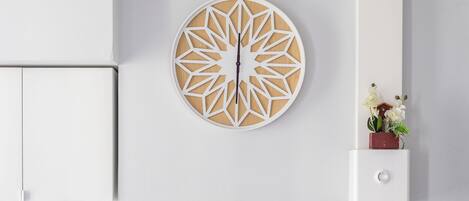 Un mur moderne agrémenté d’une horloge géométrique, d’une petite plante et d’un meuble blanc.