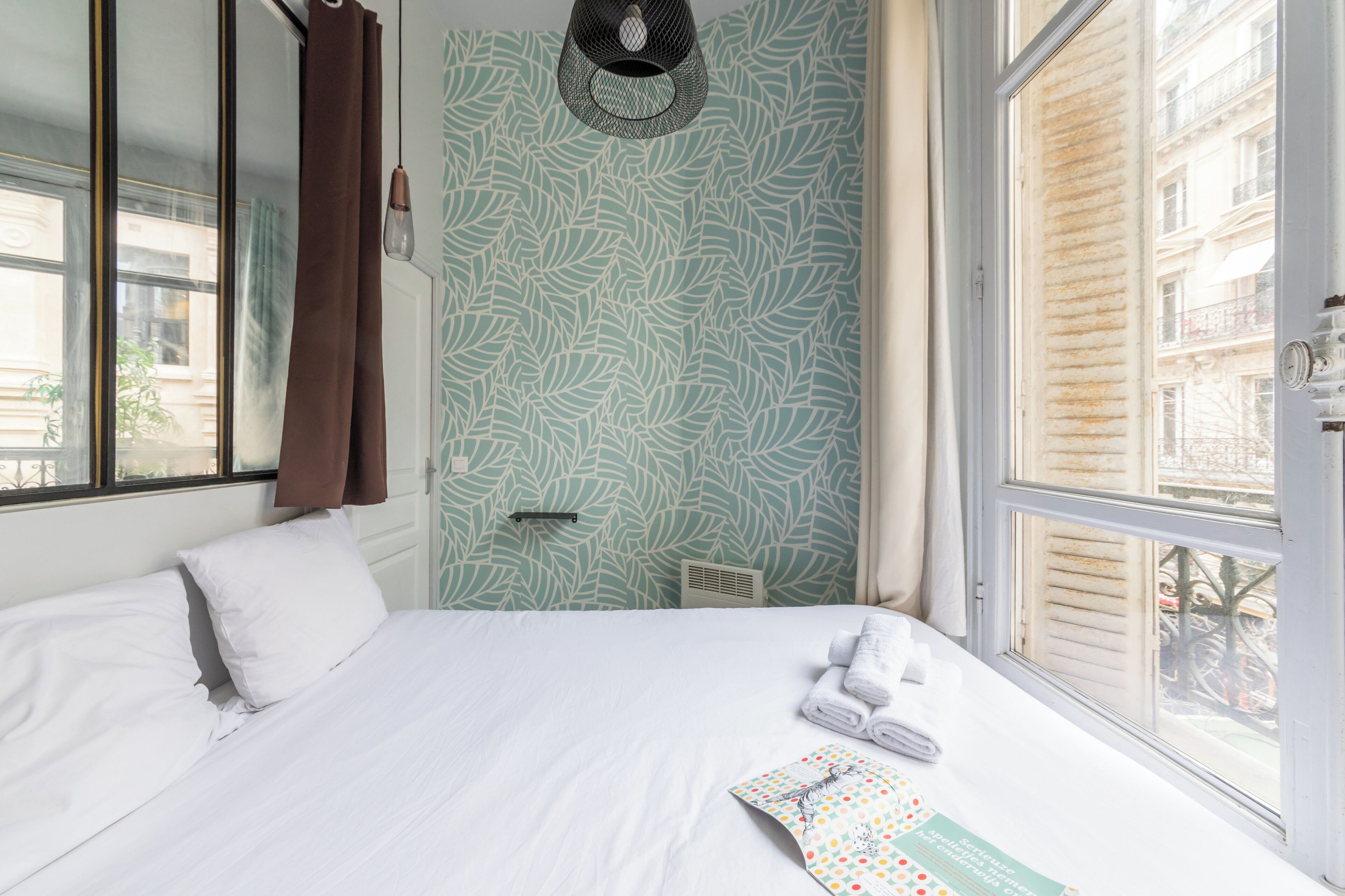 Une chambre d’hôtel avec un lit, une fenêtre et un mur orné d’un motif végétal.